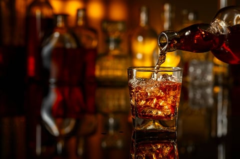 Whiskey being poured from a bottle into a glass with ice on a black reflective background