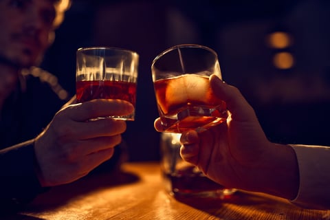 Two hands raising whiskey glasses for evening toast - shared bar rituals