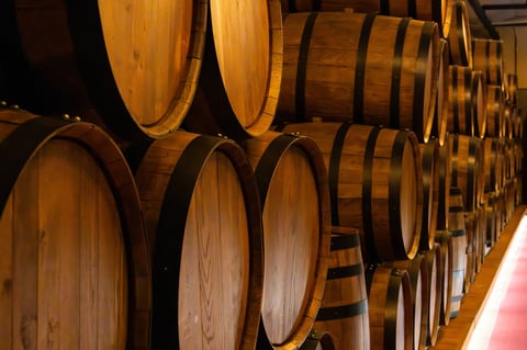 Close-up of stacked wooden barrels with iron hoops inside a dimly lit aging cellar