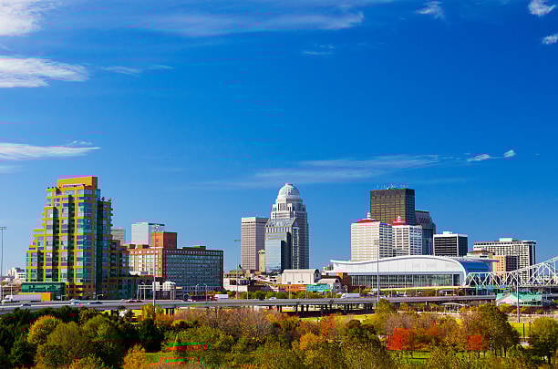 Cincinnati skyline with modern buildings and bridges over trees on a clear blue sky day