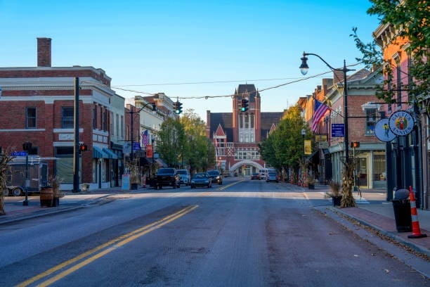 Historic downtown street with brick buildings, storefronts, traffic light, and church tower in background under clear blue sky