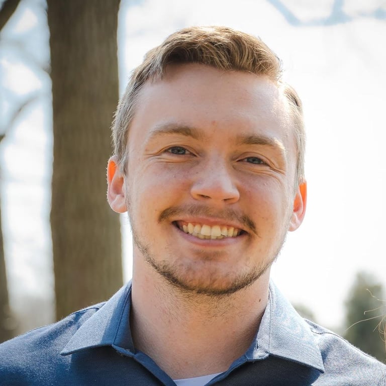 Smiling man with blonde hair wearing a blue shirt, photographed outdoors near a tree trunk - James Johnson, founder of The Barrel Blueprint